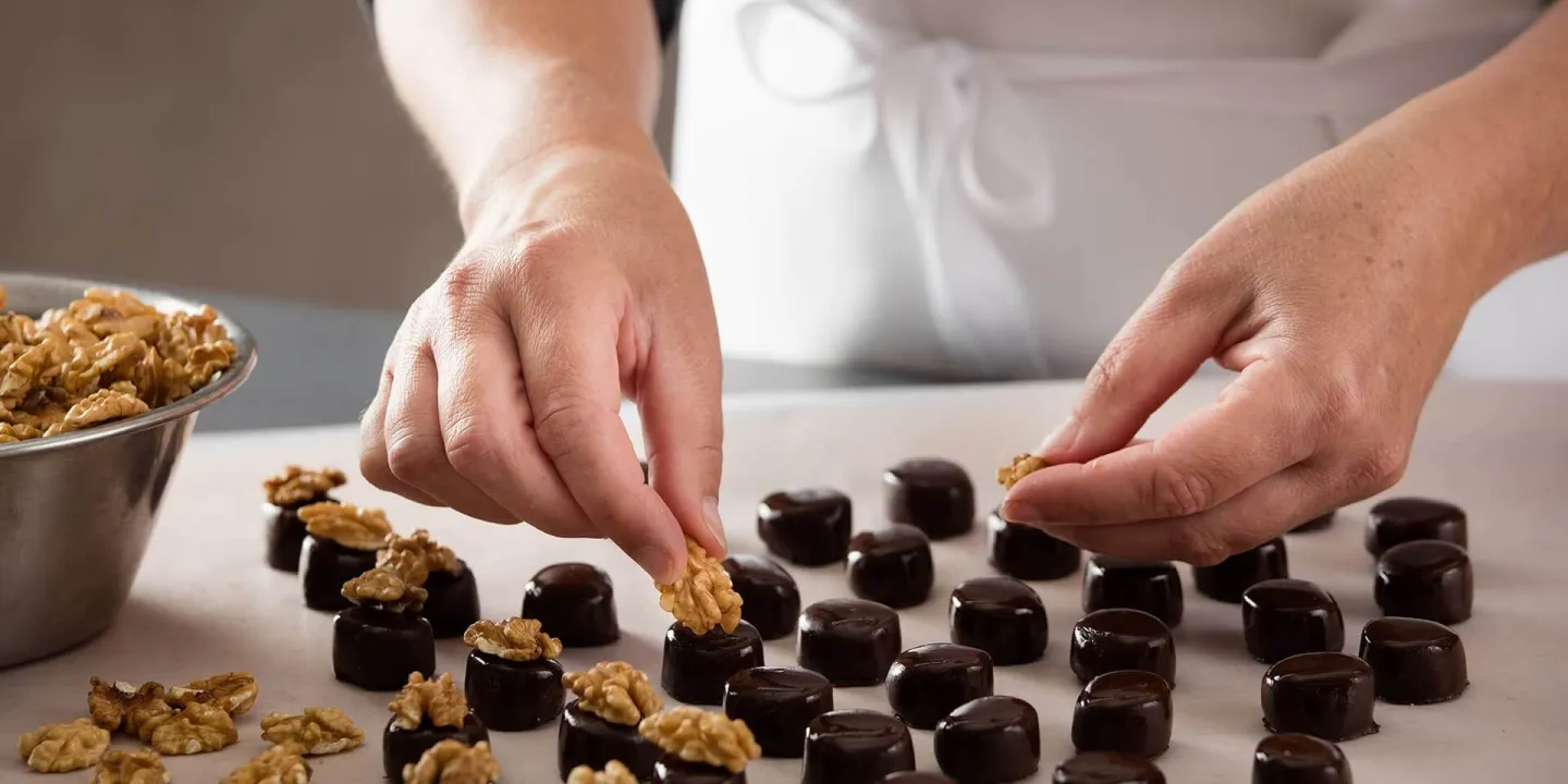 Produktionsaufnahme: Halbe Walnüsse werden von Hand auf Walnuss Marzipan Pralinen gelegt